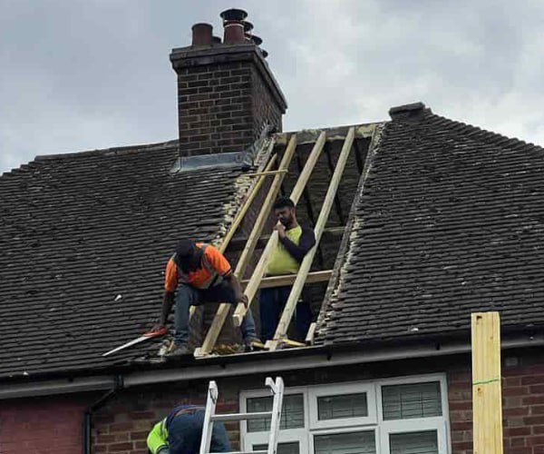 This is a photo of a roof repair being carried out. A section of the roof has been stripped and two roofers are replacing the rafters. Works being carried out by DHT Roofing Cudworth